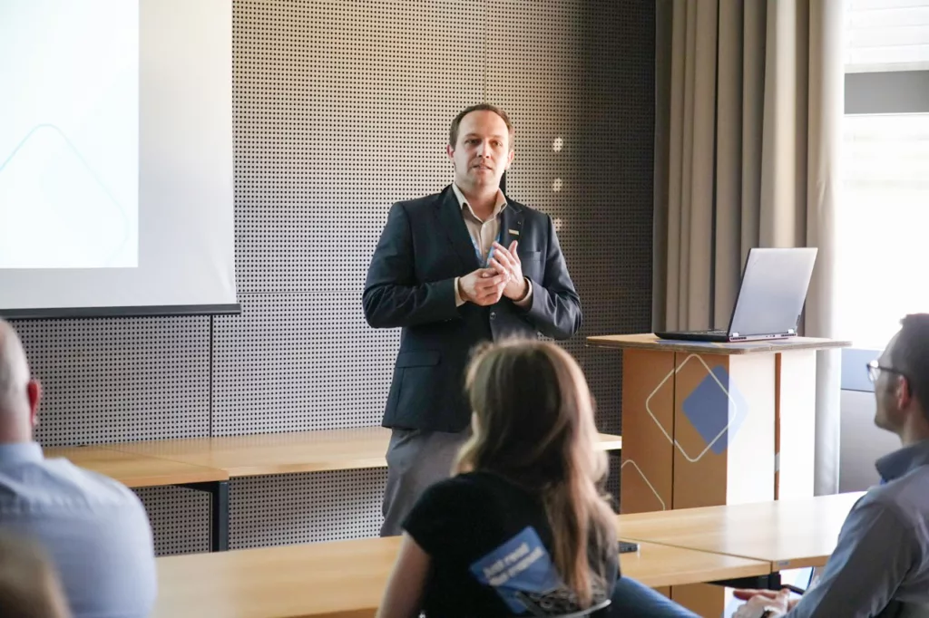 Mann spricht vor Publikum in Konferenzraum.